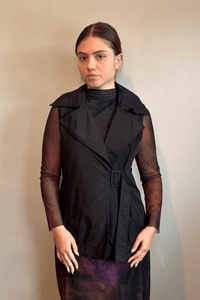 Kozan black A-line sleeveless vest with wide notched lapels, a wrap-style front, and adjustable self-belt with covered rectangular buckle.