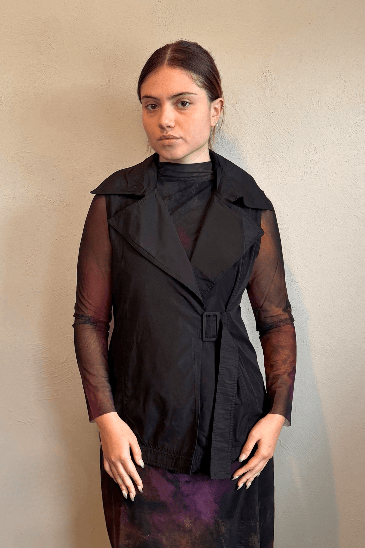 Kozan black A-line sleeveless vest with wide notched lapels, a wrap-style front, and adjustable self-belt with covered rectangular buckle.