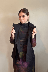 Kozan black A-line sleeveless vest with wide notched lapels, a wrap-style front, and adjustable self-belt with covered rectangular buckle.