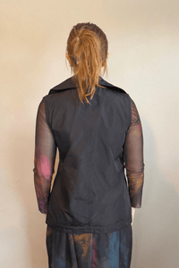 Kozan black A-line sleeveless vest with wide notched lapels, a wrap-style front, and adjustable self-belt with covered rectangular buckle.