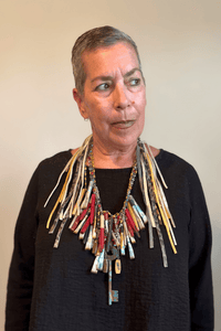 A Rare Bird Painter's Palette Layered Necklace, a wide bib-style statement necklace with layered paint-marked brushes, colorful beads, chains, dangling artist-inspired objects, and long mixed leather fringe ties.
