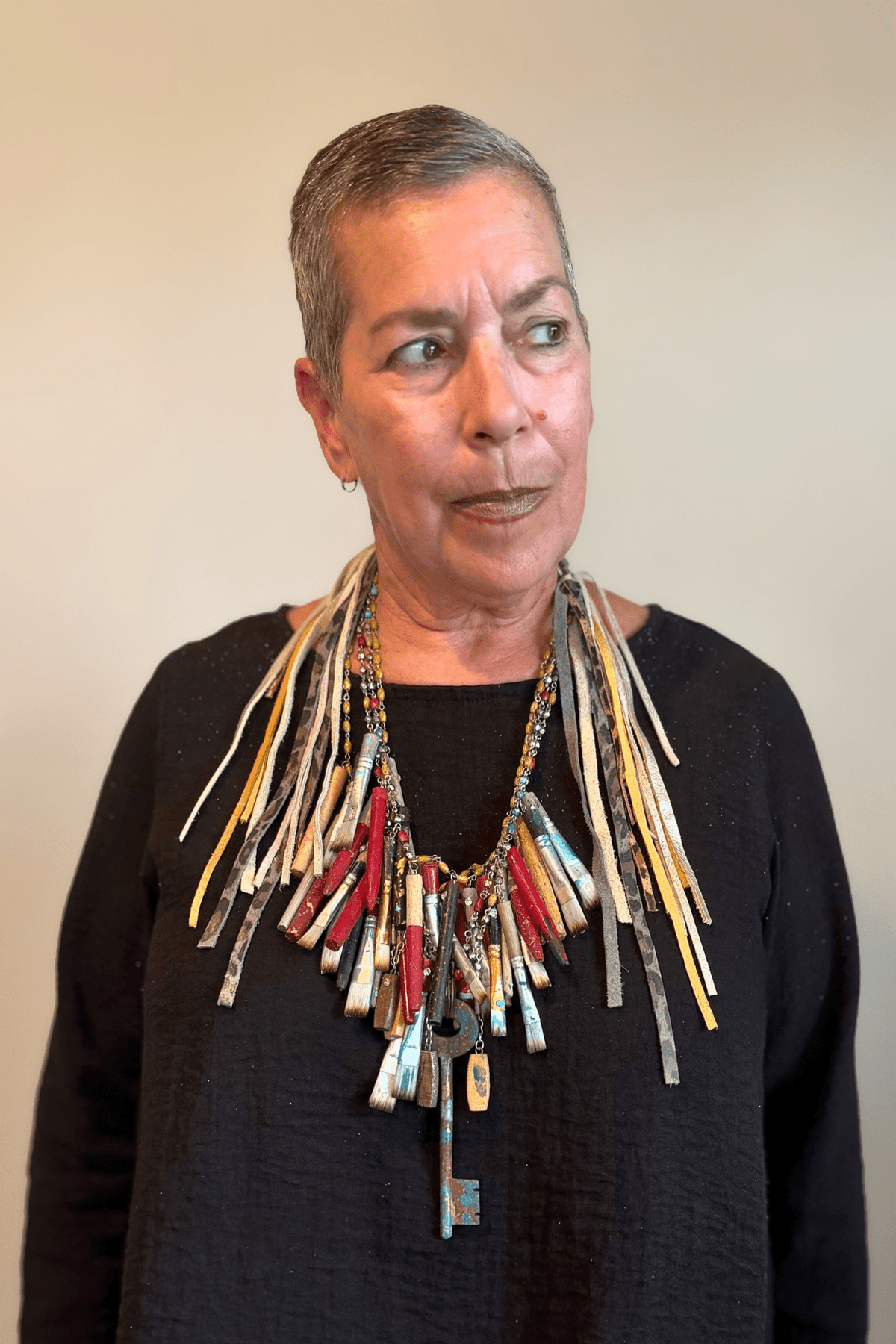 A Rare Bird Painter's Palette Layered Necklace, a wide bib-style statement necklace with layered paint-marked brushes, colorful beads, chains, dangling artist-inspired objects, and long mixed leather fringe ties.