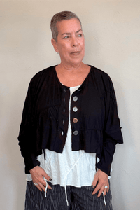 Cropped knit cardigan jacket shown in black and white, with a relaxed boxy shape, dropped shoulders, long sleeves, assorted front buttons, curved seam detailing, raw-edge finishes, and hanging cord accents.