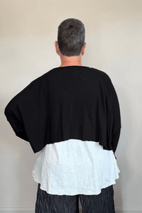 Cropped knit cardigan jacket shown in black and white, with a relaxed boxy shape, dropped shoulders, long sleeves, assorted front buttons, curved seam detailing, raw-edge finishes, and hanging cord accents.