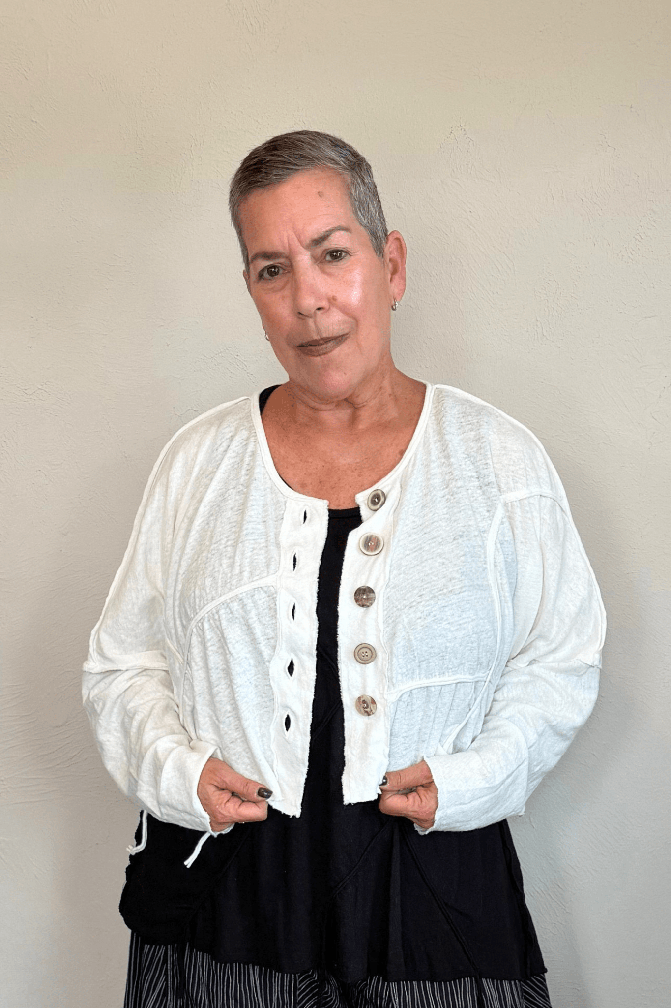 Cropped knit cardigan jacket shown in black and white, with a relaxed boxy shape, dropped shoulders, long sleeves, assorted front buttons, curved seam detailing, raw-edge finishes, and hanging cord accents.