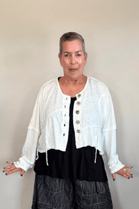 Cropped knit cardigan jacket shown in black and white, with a relaxed boxy shape, dropped shoulders, long sleeves, assorted front buttons, curved seam detailing, raw-edge finishes, and hanging cord accents.