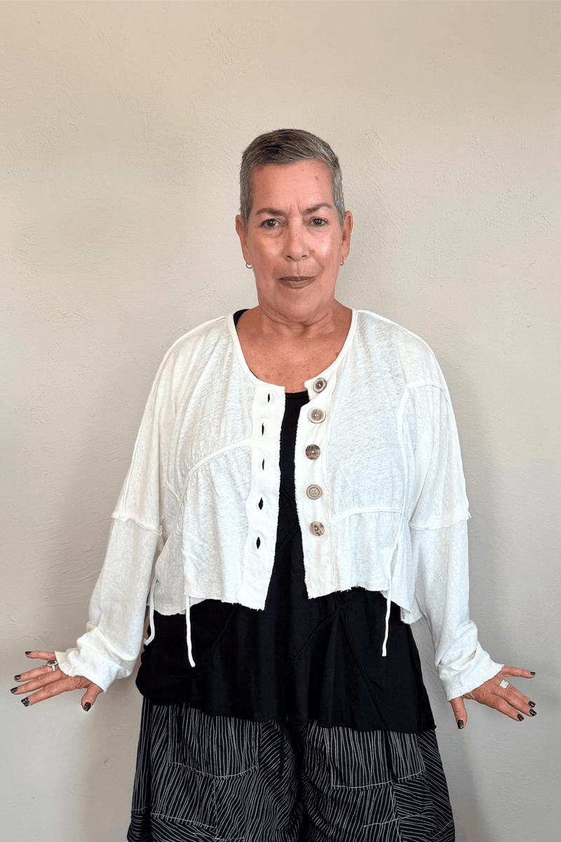 Cropped knit cardigan jacket shown in black and white, with a relaxed boxy shape, dropped shoulders, long sleeves, assorted front buttons, curved seam detailing, raw-edge finishes, and hanging cord accents.
