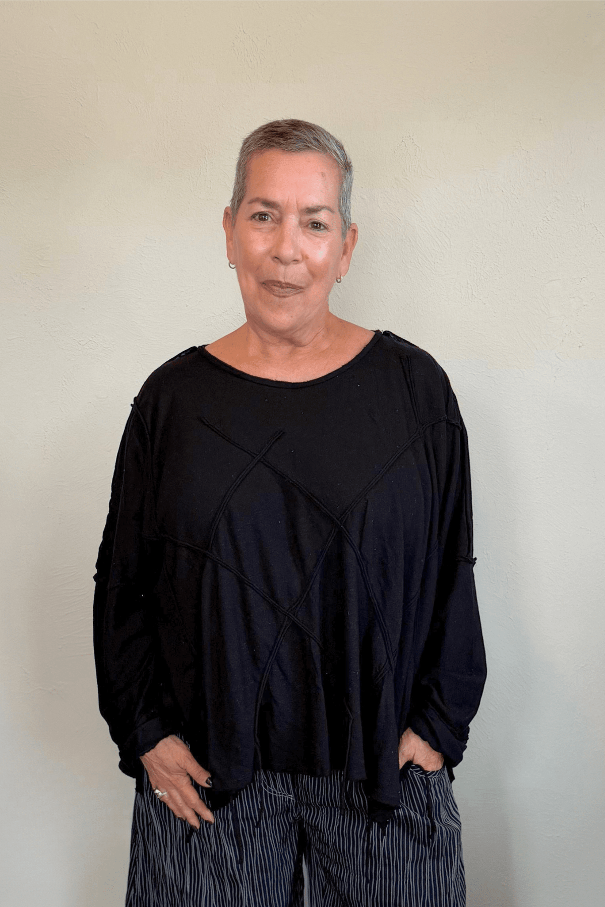 Oversized long-sleeve corded top shown in black and white, with a wide round neckline, dropped shoulders, abstract raised cord detailing across the front, an uneven raw-edge hem, and hanging cord accents.