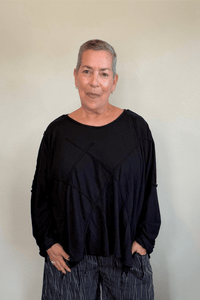 Oversized long-sleeve corded top shown in black and white, with a wide round neckline, dropped shoulders, abstract raised cord detailing across the front, an uneven raw-edge hem, and hanging cord accents.