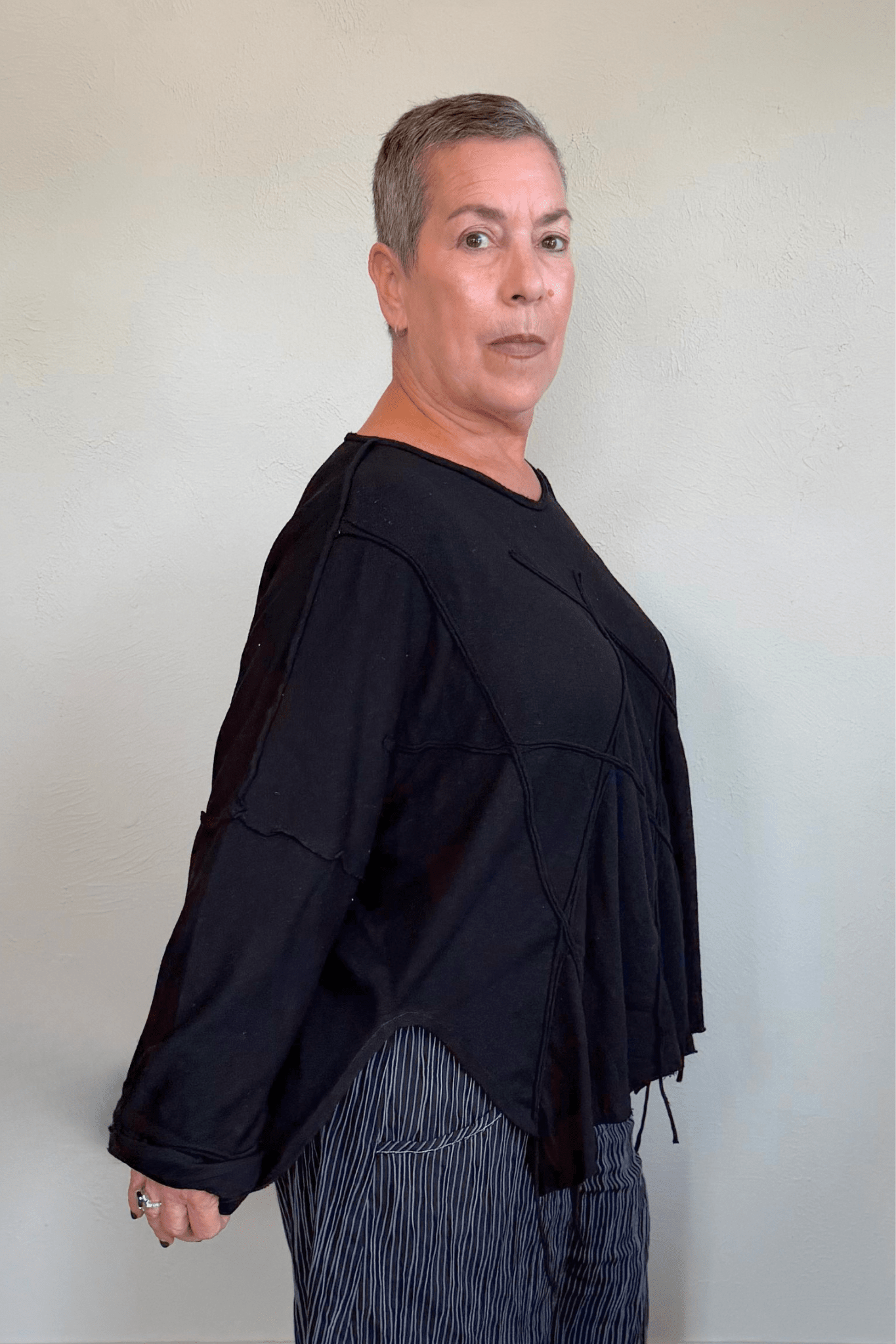 Oversized long-sleeve corded top shown in black and white, with a wide round neckline, dropped shoulders, abstract raised cord detailing across the front, an uneven raw-edge hem, and hanging cord accents.