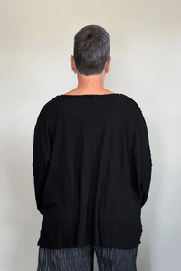 Oversized long-sleeve corded top shown in black and white, with a wide round neckline, dropped shoulders, abstract raised cord detailing across the front, an uneven raw-edge hem, and hanging cord accents.