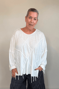 Oversized long-sleeve corded top shown in black and white, with a wide round neckline, dropped shoulders, abstract raised cord detailing across the front, an uneven raw-edge hem, and hanging cord accents.
