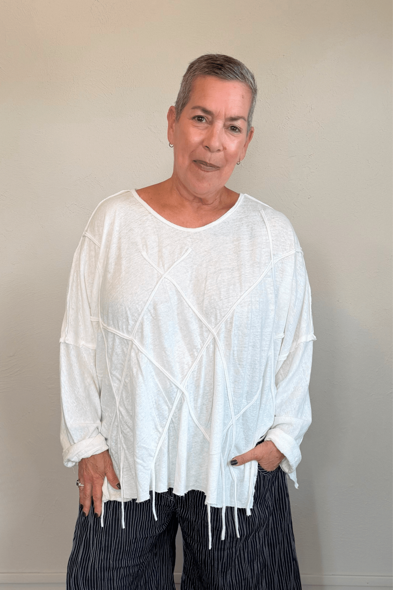 Oversized long-sleeve corded top shown in black and white, with a wide round neckline, dropped shoulders, abstract raised cord detailing across the front, an uneven raw-edge hem, and hanging cord accents.