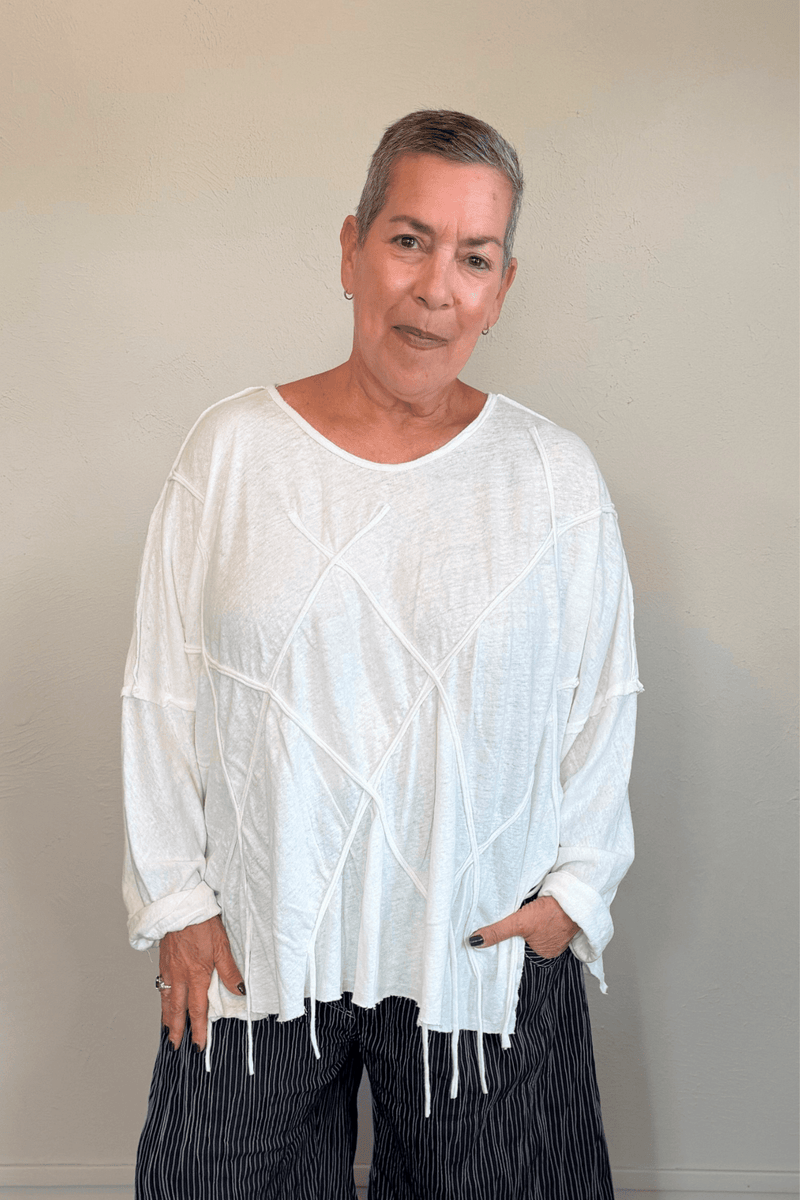 Oversized long-sleeve corded top shown in black and white, with a wide round neckline, dropped shoulders, abstract raised cord detailing across the front, an uneven raw-edge hem, and hanging cord accents.