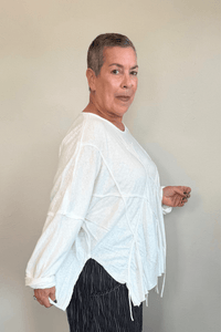 Oversized long-sleeve corded top shown in black and white, with a wide round neckline, dropped shoulders, abstract raised cord detailing across the front, an uneven raw-edge hem, and hanging cord accents.
