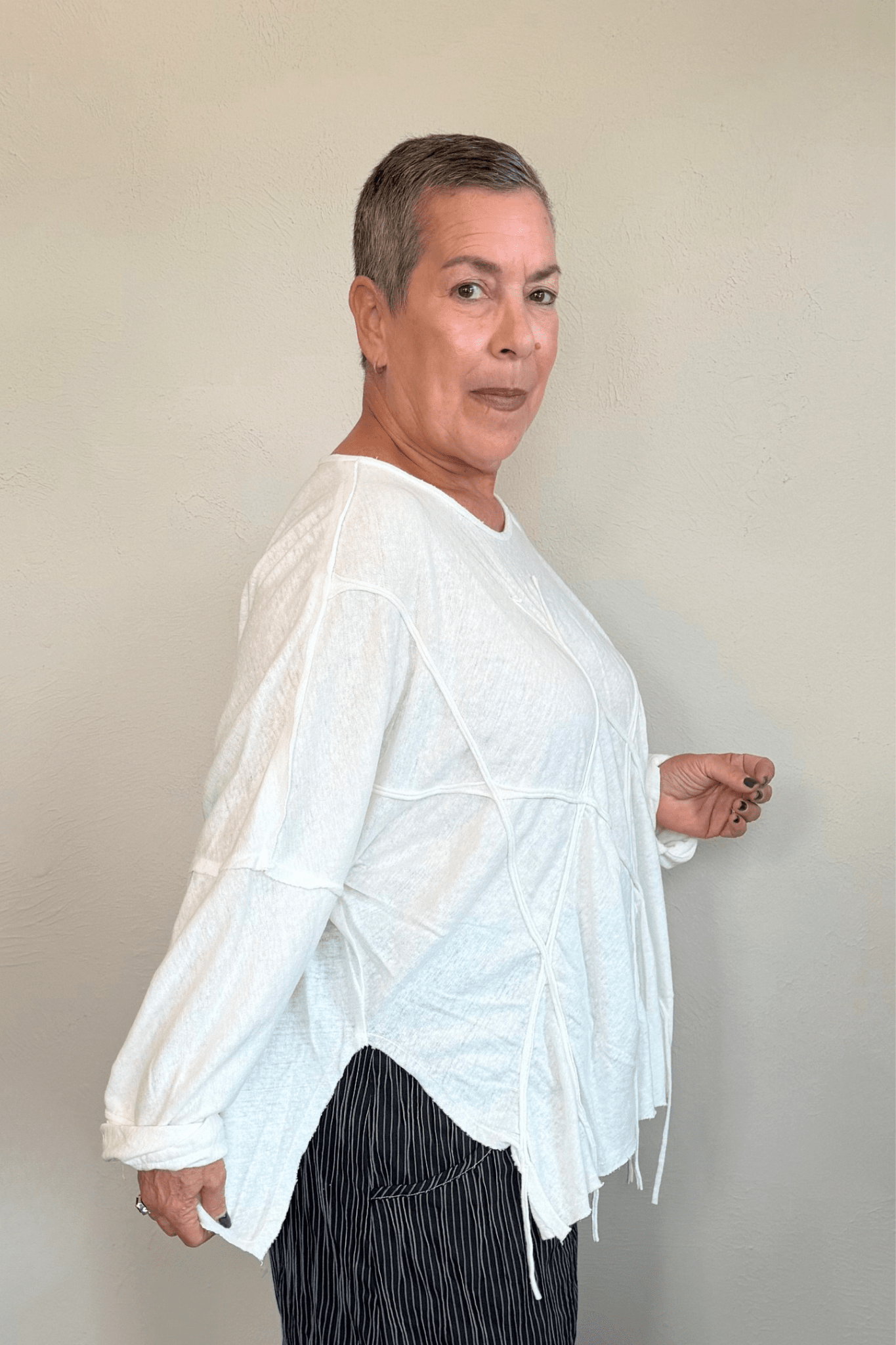 Oversized long-sleeve corded top shown in black and white, with a wide round neckline, dropped shoulders, abstract raised cord detailing across the front, an uneven raw-edge hem, and hanging cord accents.
