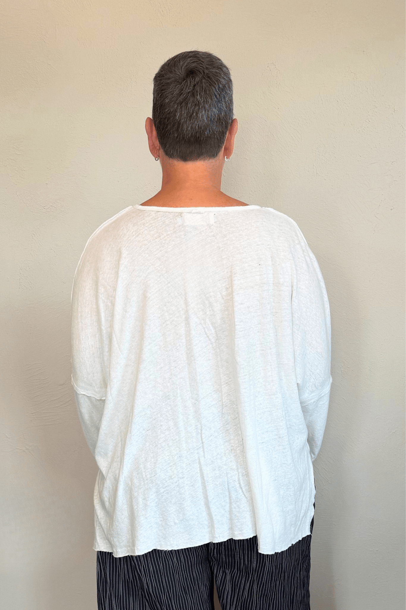 Oversized long-sleeve corded top shown in black and white, with a wide round neckline, dropped shoulders, abstract raised cord detailing across the front, an uneven raw-edge hem, and hanging cord accents.
