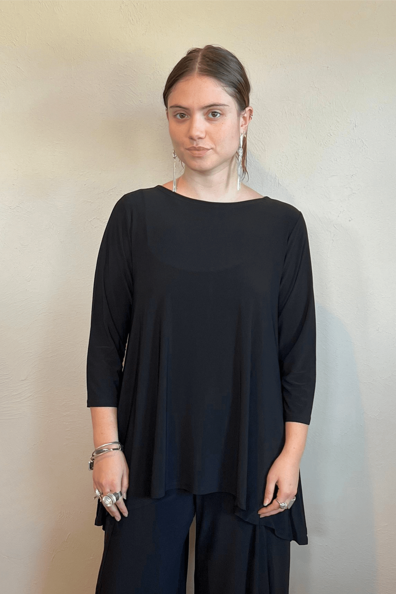 Model wearing the black Kozan Dima tunic with a boat neckline, three-quarter sleeves, and an asymmetrical draped hem, shown from front and back.
