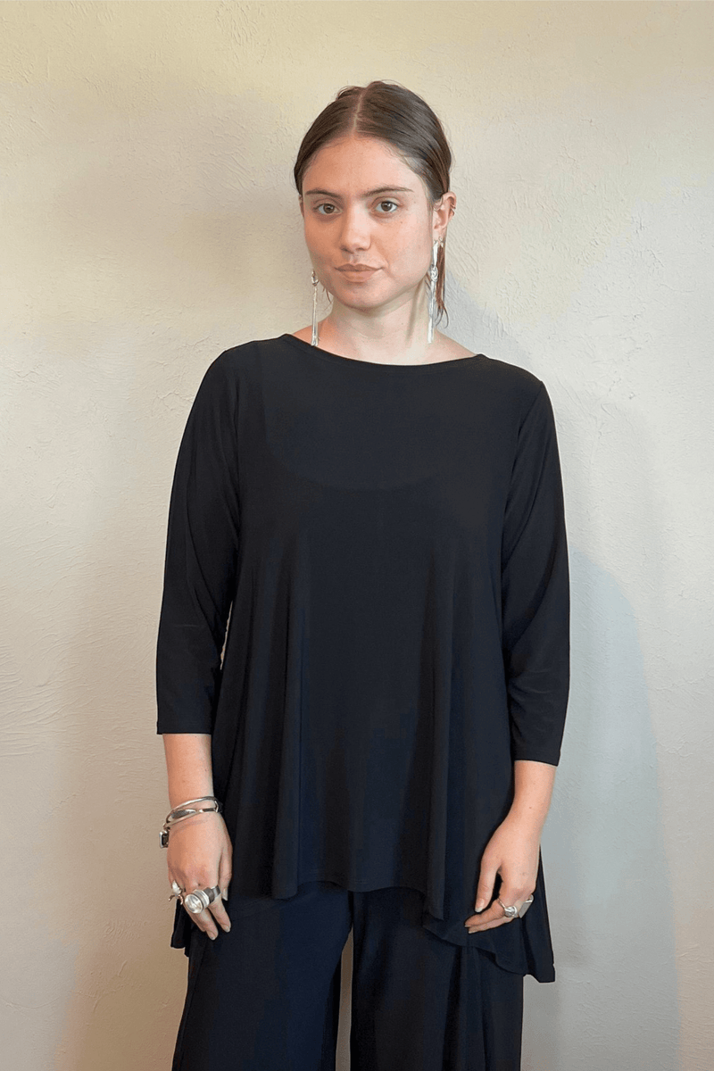 Model wearing the black Kozan Dima tunic with a boat neckline, three-quarter sleeves, and an asymmetrical draped hem, shown from front and back.