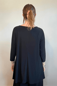 Model wearing the black Kozan Dima tunic with a boat neckline, three-quarter sleeves, and an asymmetrical draped hem, shown from front and back.