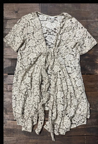 Ivory floral lace layering jacket with elbow-length sleeves, long tie-front closure, gathered shaping, and a flowing high-low hem with ruffled edge.