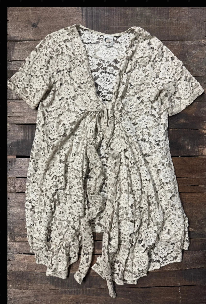 Ivory floral lace layering jacket with elbow-length sleeves, long tie-front closure, gathered shaping, and a flowing high-low hem with ruffled edge.