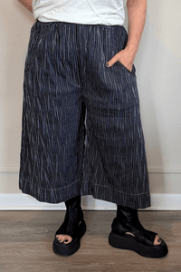 Black cropped wide-leg pants with fine vertical white striping, pull-on elastic waistband, angled side pockets, and contrast topstitching at the hem and pocket edges.