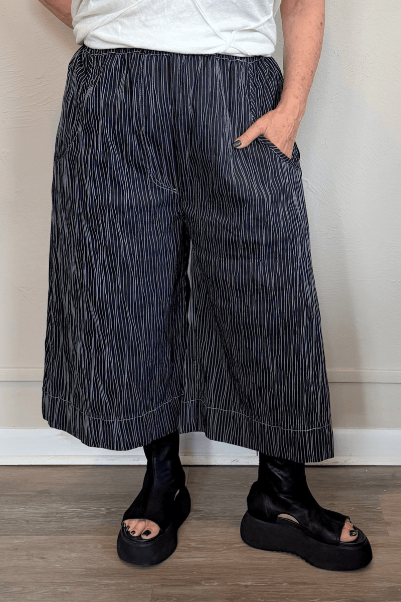 Black cropped wide-leg pants with fine vertical white striping, pull-on elastic waistband, angled side pockets, and contrast topstitching at the hem and pocket edges.