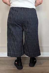 Black cropped wide-leg pants with fine vertical white striping, pull-on elastic waistband, angled side pockets, and contrast topstitching at the hem and pocket edges.