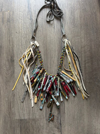 A Rare Bird Painter's Palette Layered Necklace, a wide bib-style statement necklace with layered paint-marked brushes, colorful beads, chains, dangling artist-inspired objects, and long mixed leather fringe ties.