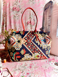 Atenti Sew Crewel Pioneer handbag with multicolor crewel-style embroidery, bright red double handles, and structured snap-frame silhouette