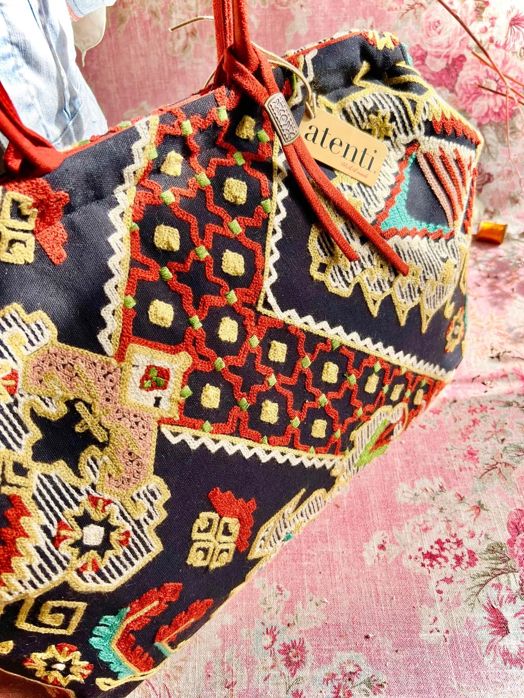 Atenti Sew Crewel Pioneer handbag with multicolor crewel-style embroidery, bright red double handles, and structured snap-frame silhouette
