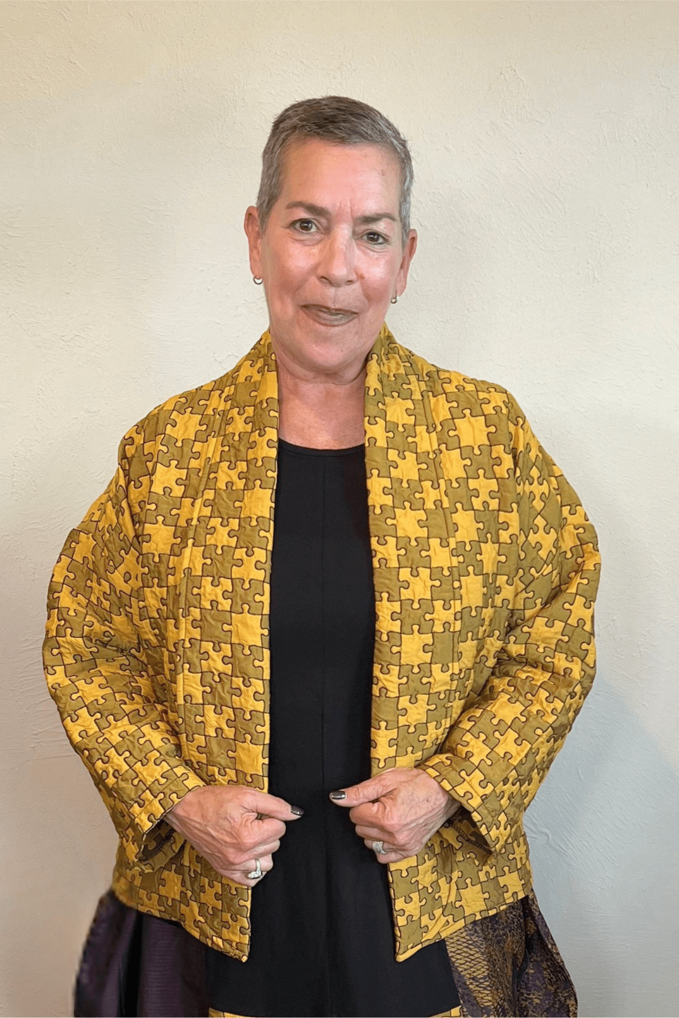 Model wearing the Kozan Sia open-front jacket with an allover mustard and olive puzzle-piece print, shown from front and back.