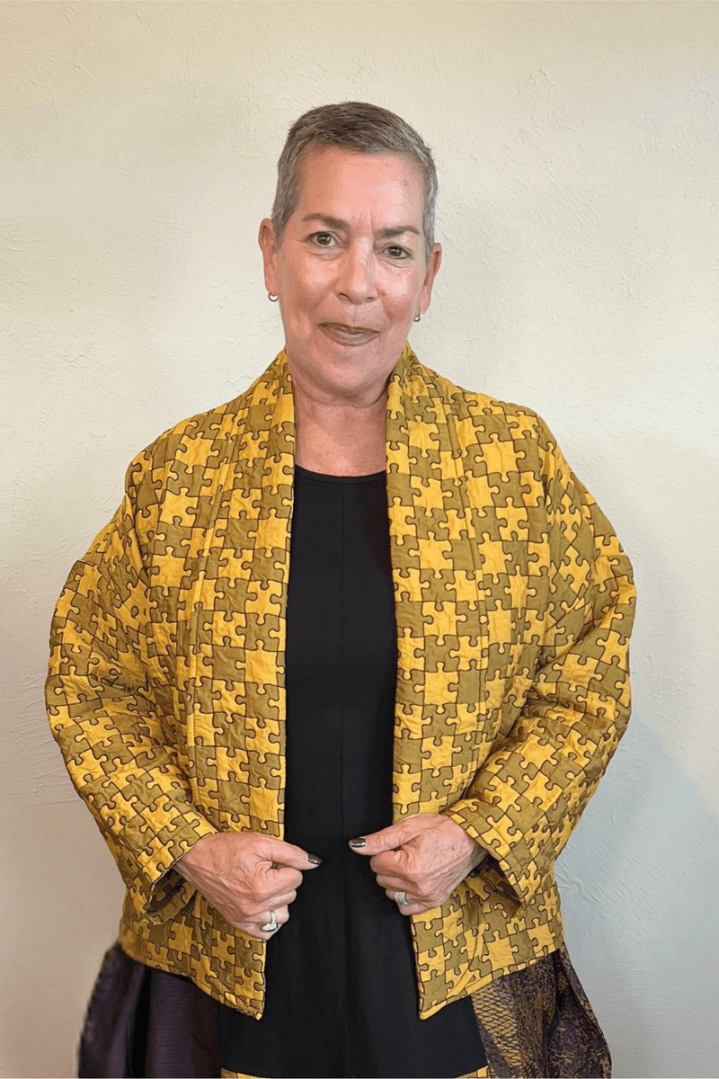 Model wearing the Kozan Sia open-front jacket with an allover mustard and olive puzzle-piece print, shown from front and back.