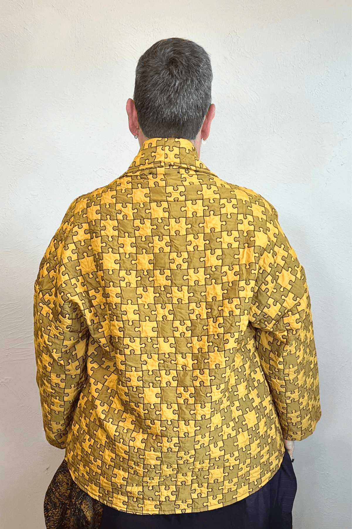 Model wearing the Kozan Sia open-front jacket with an allover mustard and olive puzzle-piece print, shown from front and back.