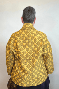 Model wearing the Kozan Sia open-front jacket with an allover mustard and olive puzzle-piece print, shown from front and back.