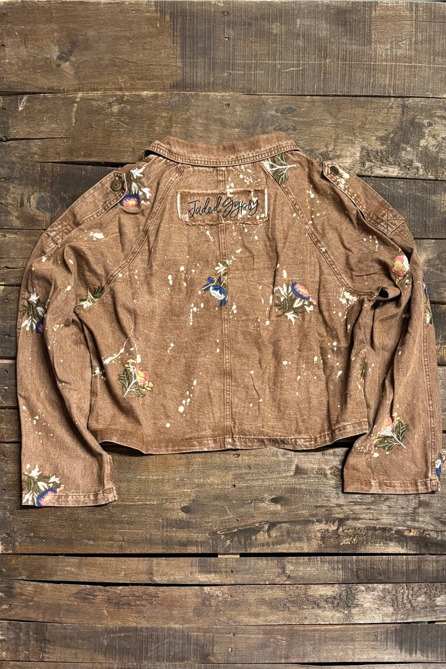 Brown cropped cotton jacket with floral embroidery, paint-splatter detailing, notched lapel collar, button front, and long sleeves with cuff tabs; back view shows center seam and Jaded Gypsy patch.